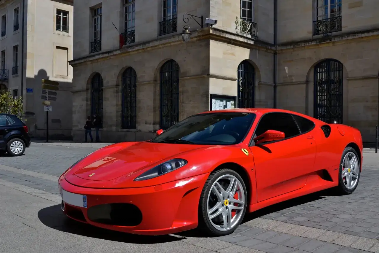 Czerwone Ferrari F430 na brukowanej ulicy. Zastanawiasz się, ile kosztuje Ferrari? To marzenie wielu kierowc&oacute;w.