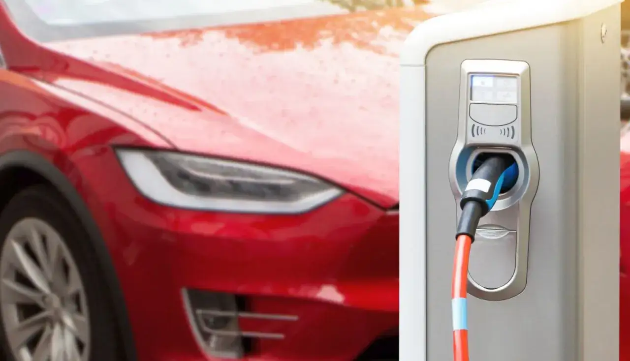 Czerwona Tesla podłączona do ładowarki. Zastanawiasz się, jak długo ładuje się Tesla? Czas zależy od modelu i ładowarki.