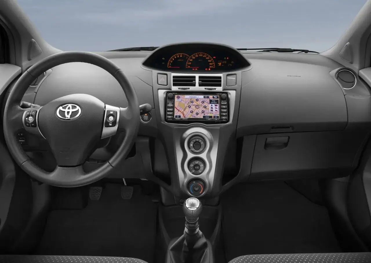 Wnętrze Toyoty Yaris 2 z nawigacją GPS, kierownicą i dźwignią zmiany biegów.
