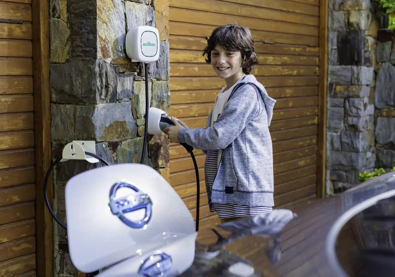 Chłopiec podłącza samoch&oacute;d elektryczny do ładowarki Wallbox. Dowiedz się, ile kosztuje ładowanie samochodu elektrycznego w domu.