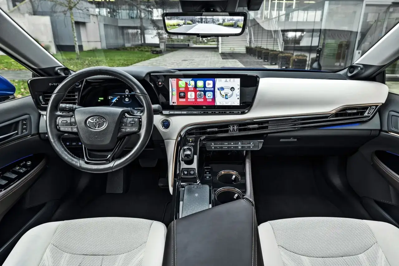 Wnętrze Toyoty Mirai. Nowoczesny kokpit z dużym ekranem dotykowym, cyfrowymi zegarami i eleganckimi detalami. Sprawdź, jaka jest toyota mirai cena.