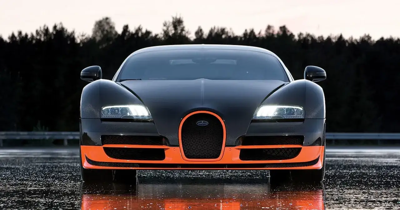Czarny Bugatti Veyron z pomarańczowymi akcentami, gotowy do przyspieszenia do 100 km/h na mokrej nawierzchni.