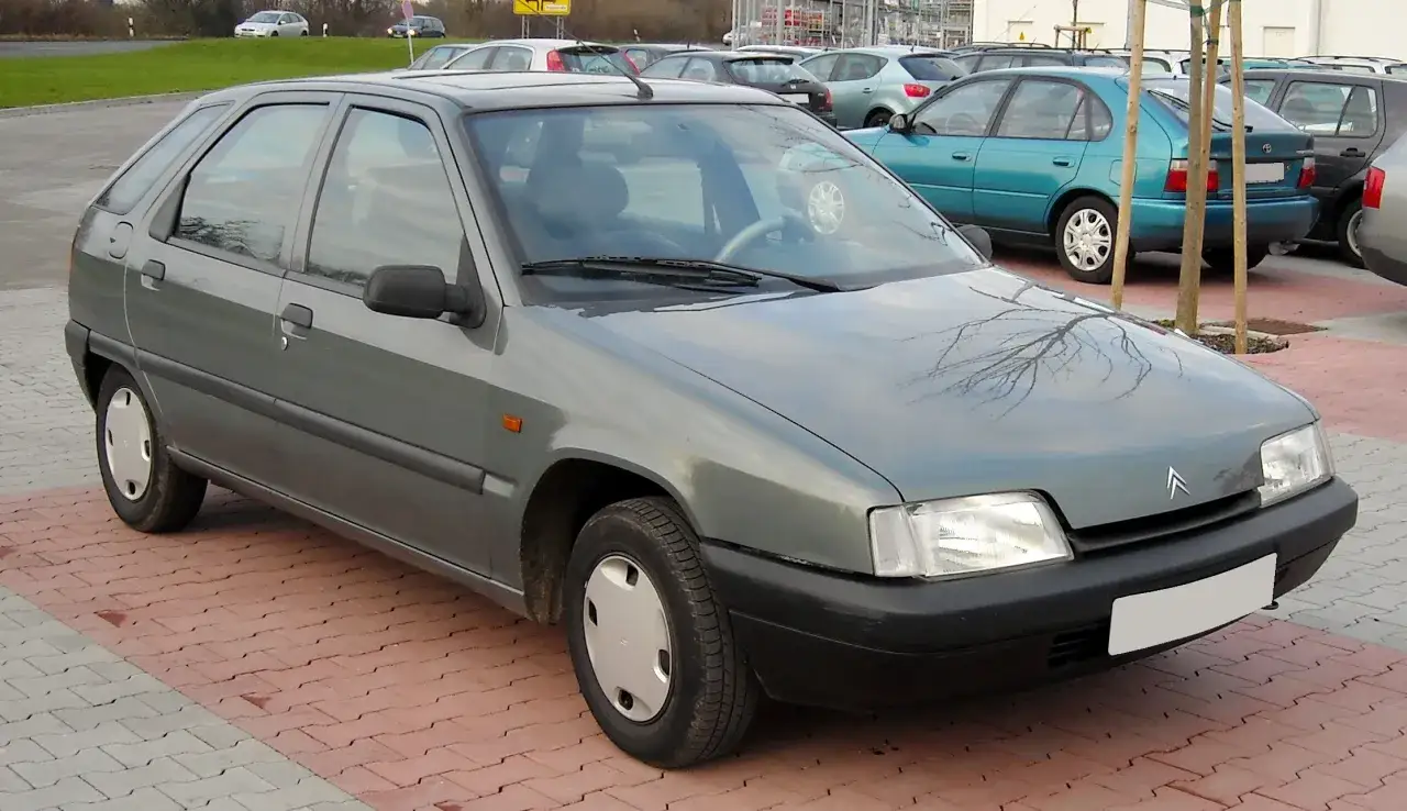 Szary Citroen ZX na parkingu. W tle inne samochody, w tym turkusowy.