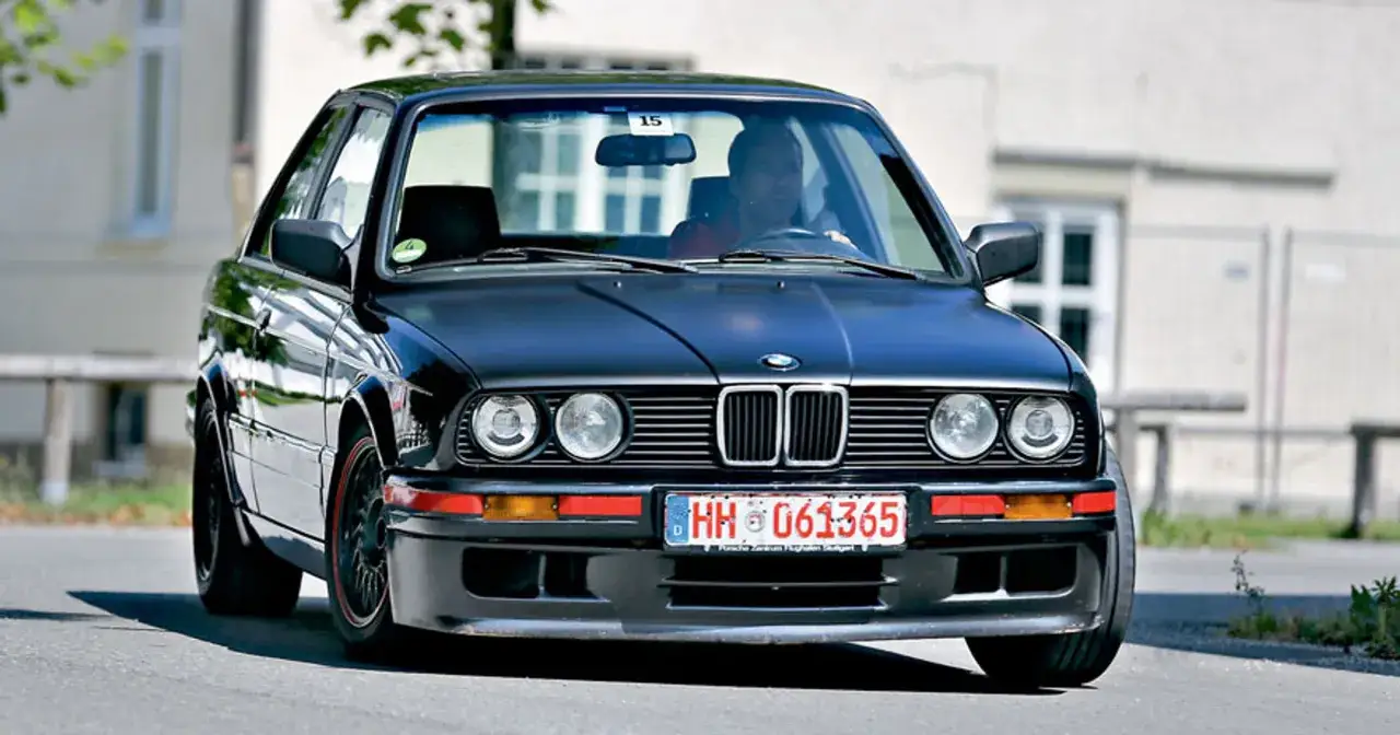 Czarny BMW E30, klasyczny youngtimer, z kierowcą za kierownicą, na drodze.