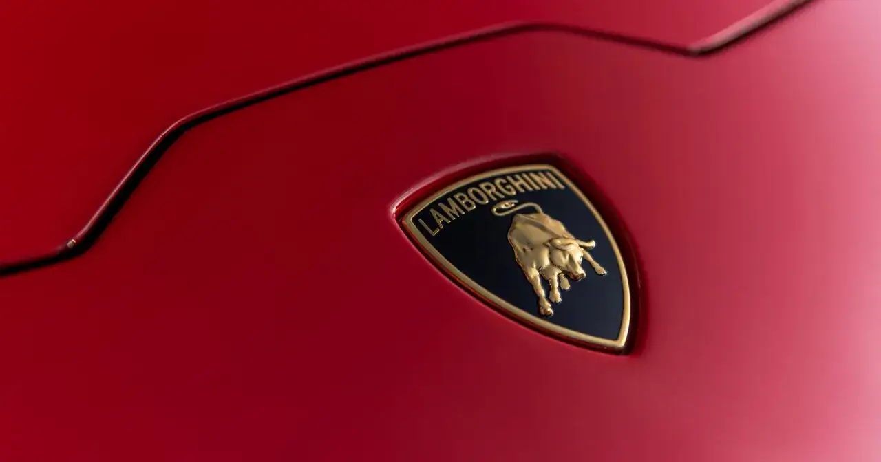 Złote logo byka na czarnym tle z napisem Lamborghini na czerwonym lakierze. To symbol mocy i szybkości, który kojarzy się z marką Lamborghini.