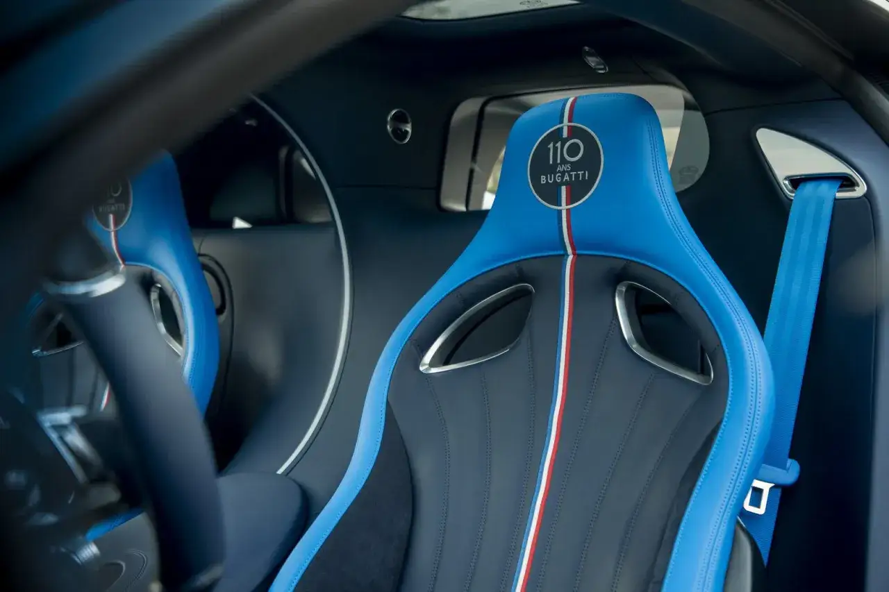Wnętrze Bugatti Chiron: niebieskie fotele z białym i czerwonym pasem, logo 110 Ans Bugatti.