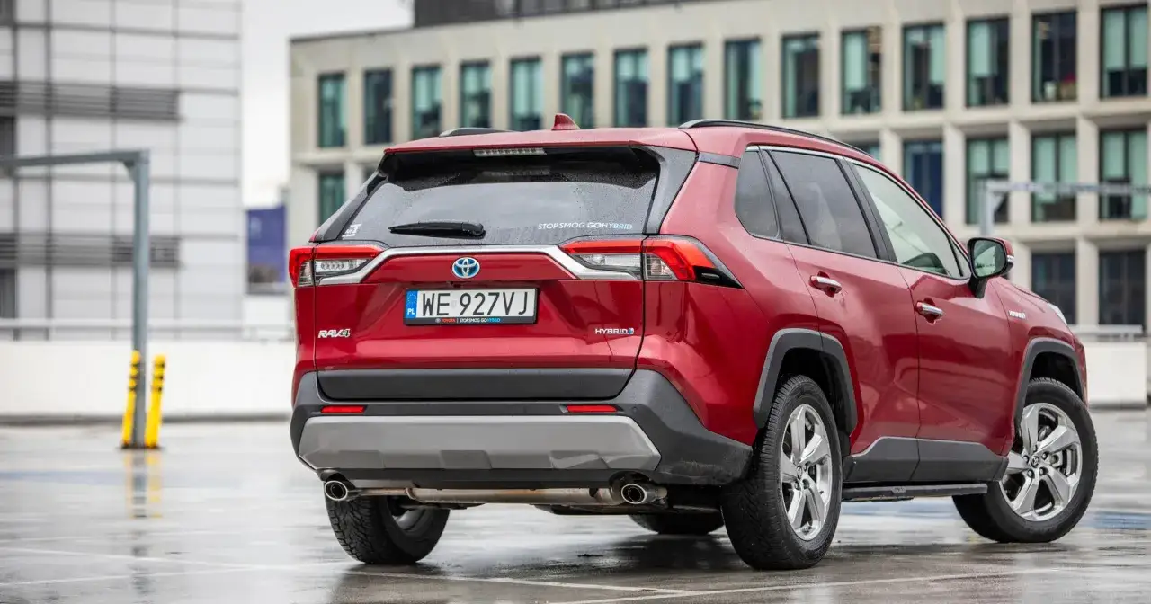 Czerwona Toyota RAV4 Hybrid na mokrym parkingu. Zastanawiasz się, ile pali Toyota RAV4 Hybrid? Ten model oferuje niskie spalanie.
