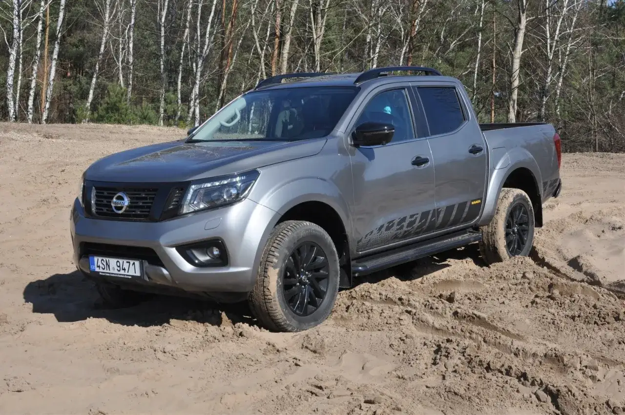 Szary Nissan Navara z czarnymi felgami i naklejkami na drzwiach pokonuje piaszczysty teren.