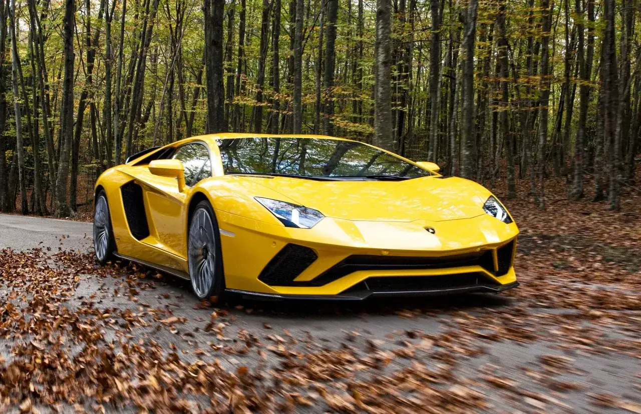 Żółte Lamborghini Aventador mknie przez jesienny las. Zastanawiasz się, ile kosztuje najtańsze Lamborghini?