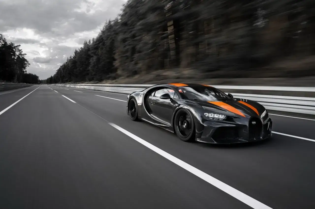 Czarny Bugatti Chiron z pomarańczowymi pasami pędzi po pustej autostradzie. Zastanawiasz się, ile koni mechanicznych ma Bugatti Chiron?