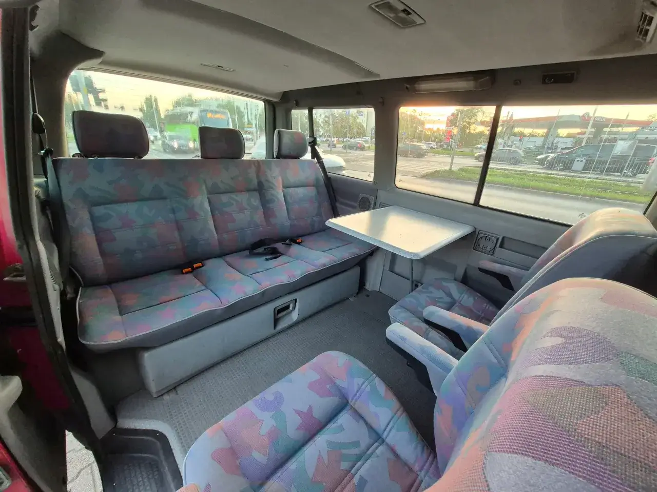 Wnętrze busa z kolorowymi siedzeniami i stolikiem. W tle widać stację Orlen i ulicę. Jaki bus w benzynie?