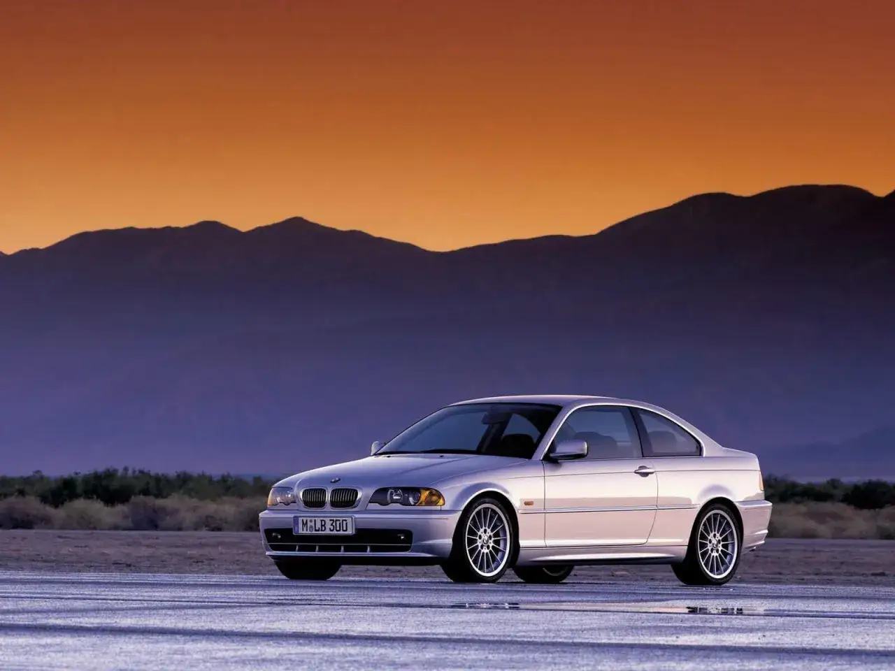 Srebrne e46 BMW coupe na pustynnej drodze o zachodzie słońca.