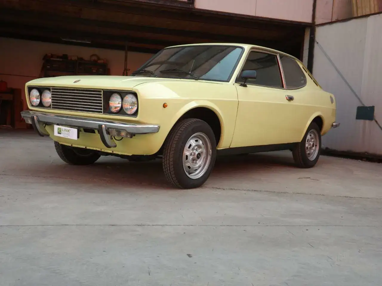 Żółty Fiat 128 coupe, klasyk z lat 70., zaparkowany w garażu.