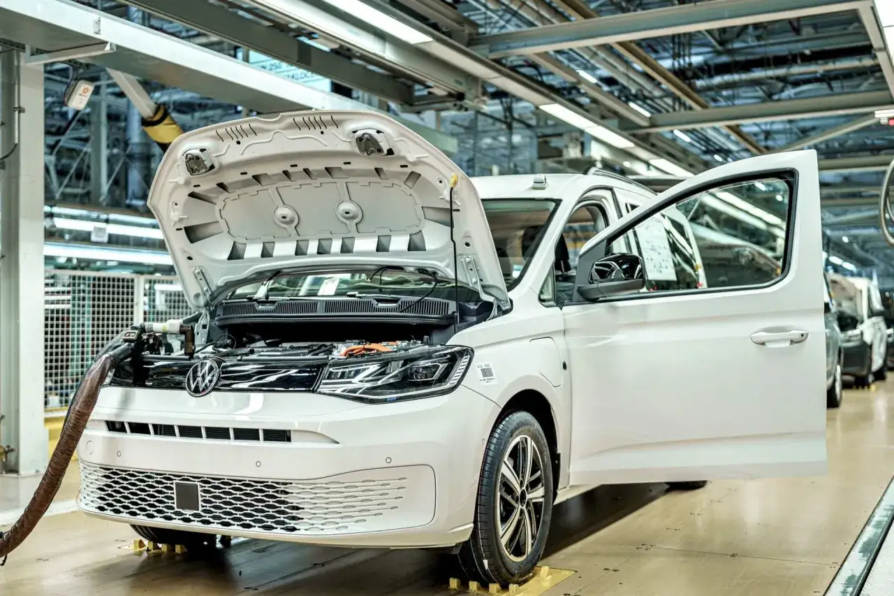 Biały samochód elektryczny na linii produkcyjnej. Widać otwartą maskę i drzwi, a także elementy silnika. Powstają tu polskie samochody.