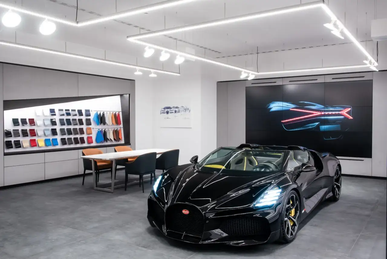 Czarny Bugatti w salonie, obok próbek kolorów i ekranu z tyłem auta. Zastanawiasz się, ile kosztuje Bugatti?
