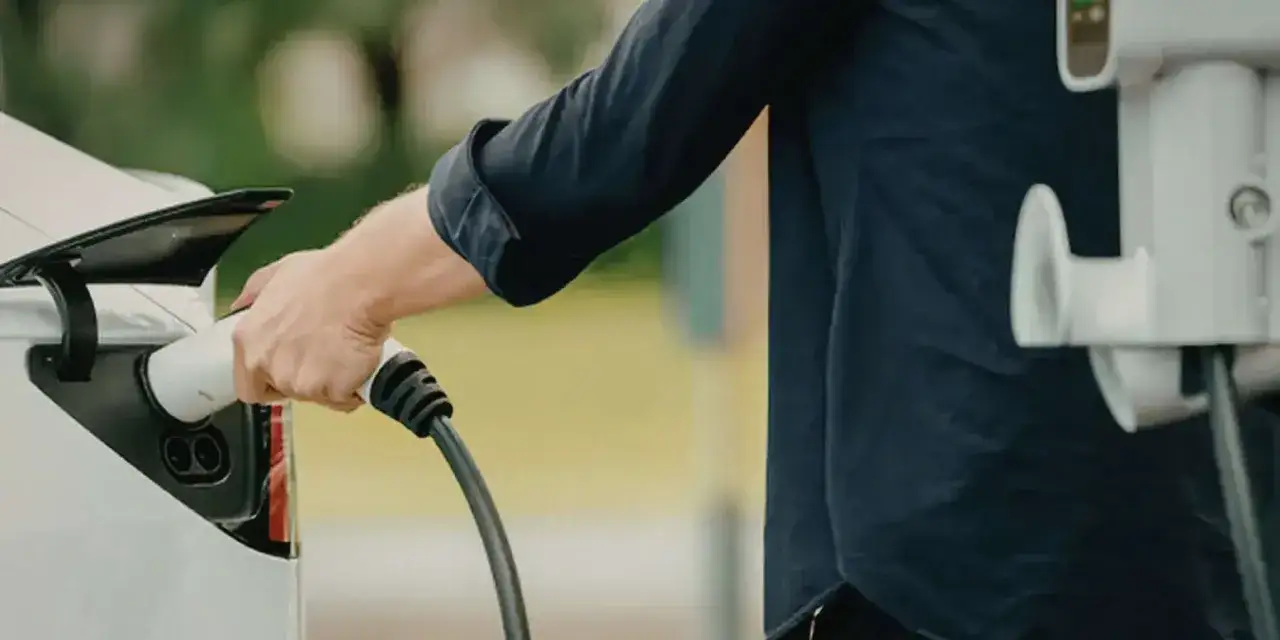 Mężczyzna podłącza ładowarkę do samochodu elektrycznego. Zastanawiasz się, ile kosztuje ładowanie samochodu elektrycznego w domu?