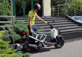 Chłopak w kasku i żółtej koszulce przy białym skuterze. Zastanawiasz się, ile kosztuje karta motorowerowa?