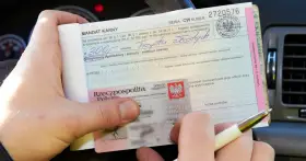 Ręka trzyma mandat karny na 300 zł i dowód osobisty. Ktoś wypełnia dokument, być może to mandat za parkowanie.