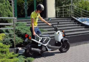 Chłopak w kasku i żółtej koszulce przy białym skuterze. Zastanawiasz się, ile kosztuje karta motorowerowa?