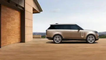 Elegancki Range Rover w kolorze piaskowym, zaparkowany przed nowoczesnym domem z drewnianymi drzwiami. Sprawdź range rover cena!