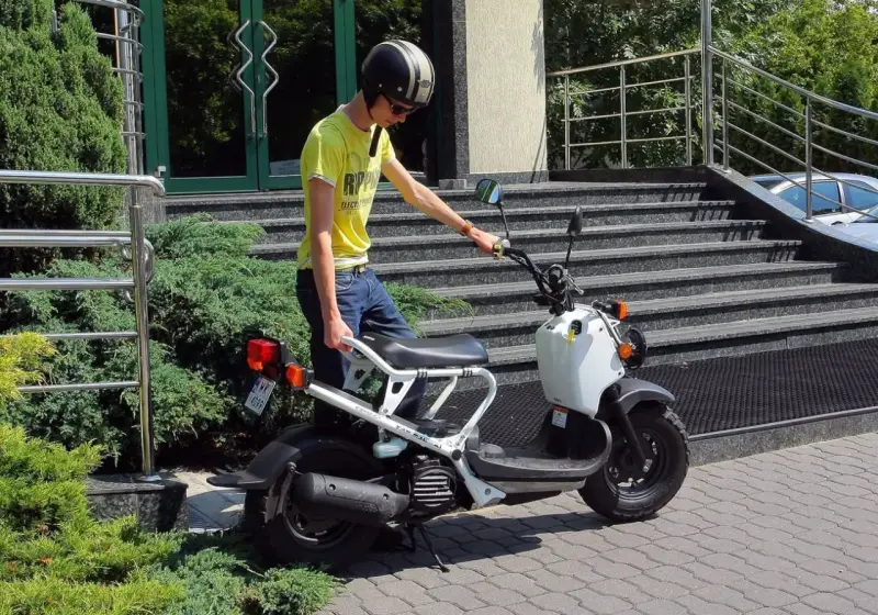 Chłopak w kasku i żółtej koszulce przy białym skuterze. Zastanawiasz się, ile kosztuje karta motorowerowa?