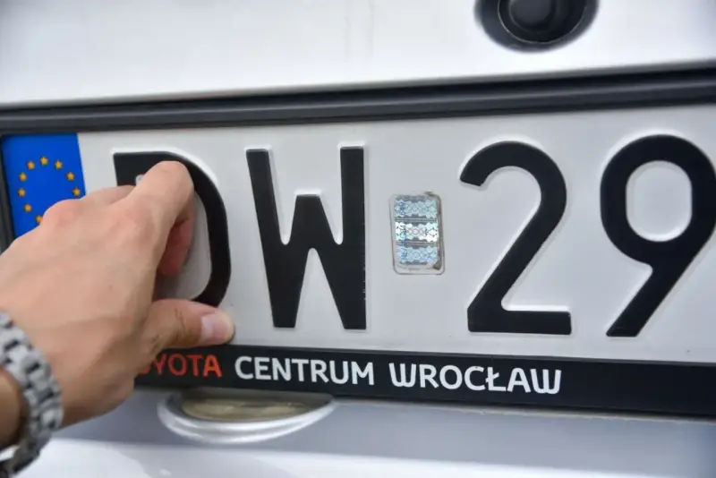 Dłoń dotyka tablicy rejestracyjnej z literami DW i numerem 29. To tablice rejestracyjne województwa dolnośląskiego.