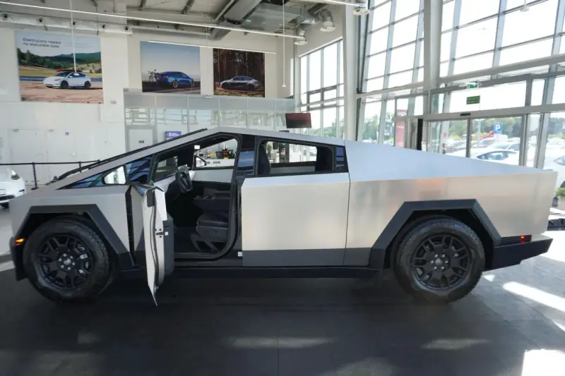 Futurystyczny Cybertruck z otwartymi drzwiami stoi w salonie. Jego kanciasta, metaliczna karoseria przyciąga wzrok.