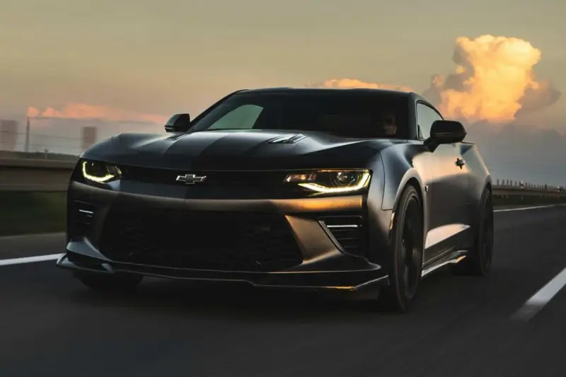 Czarny Chevrolet Camaro pędzi po autostradzie o zachodzie słońca.